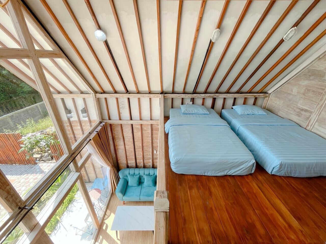 Una habitación con techo inclinado, vigas de madera, dos camas, un sofá y vistas al exterior.