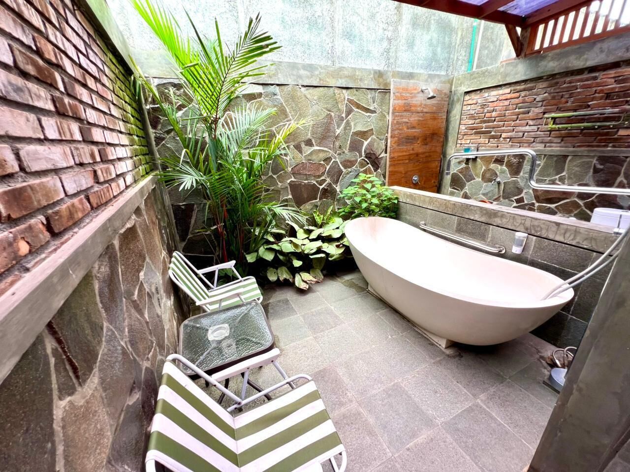 A small, enclosed bathroom with a stone wall, a brick wall, a bathtub, and a small table with chairs.