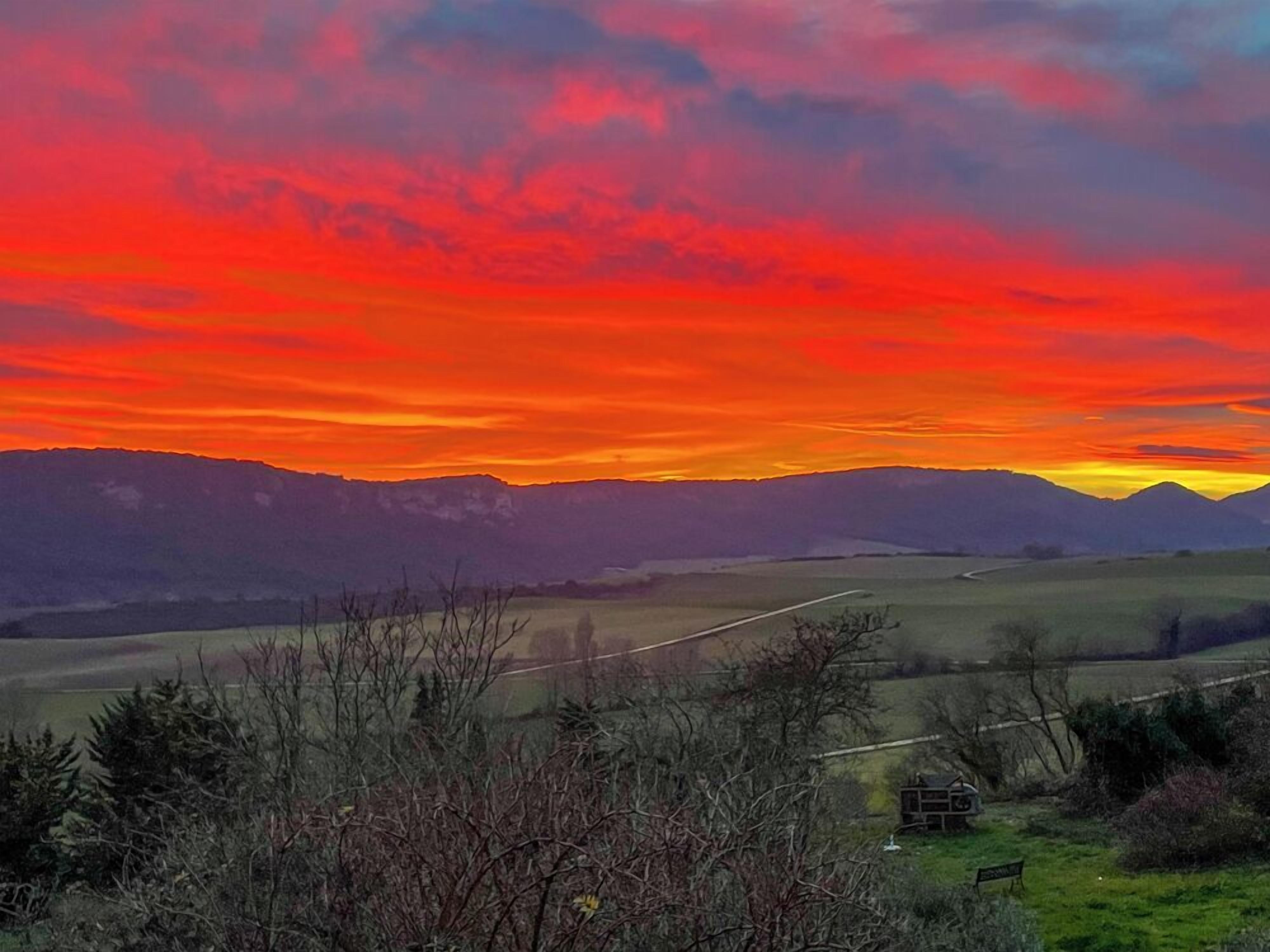 A landscape with a sunset over mountains, a road, and some vegetation.