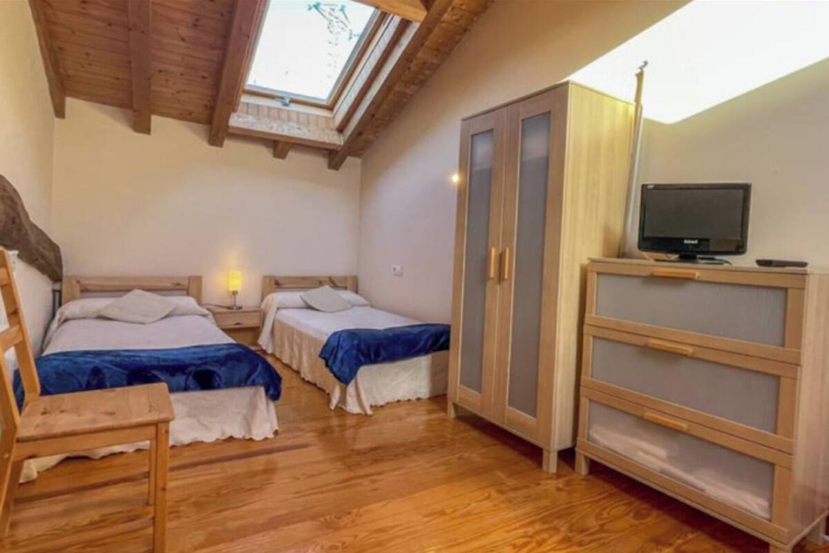 Una stanza con due letti, una sedia di legno, una TV e un armadio.