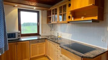 Eine Küche mit Holzausstattung, einer schwarzen Arbeitsplatte und einem Fenster mit Blick auf eine grüne Landschaft.