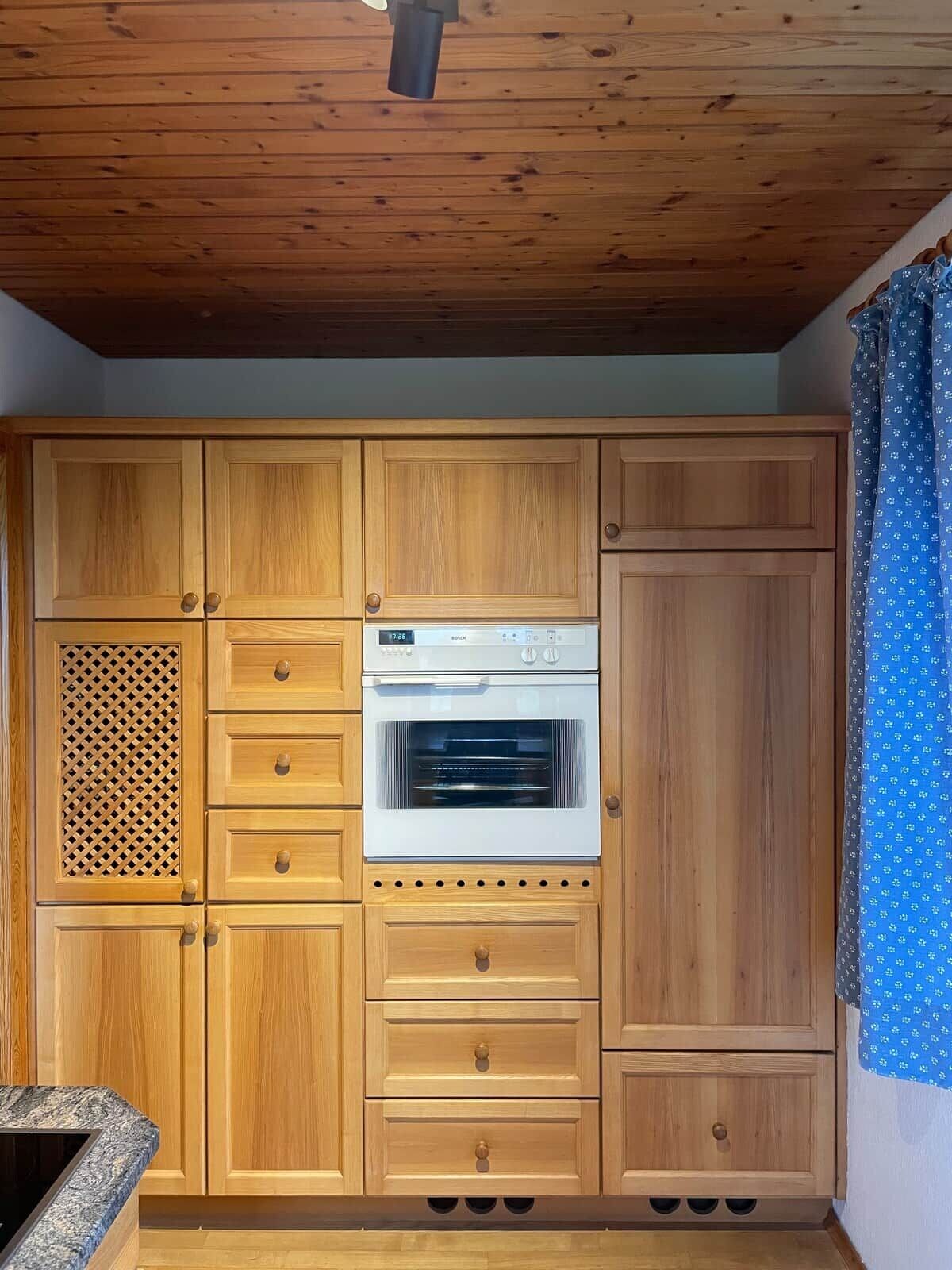 Una cucina con mobili in legno, forno a incasso e tenda a fantasia.