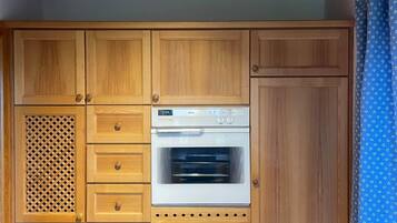 Una cucina con mobili in legno, forno a incasso e tenda a fantasia.
