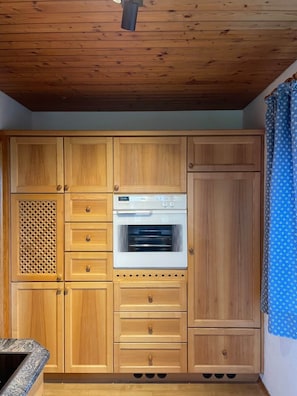 A kitchen with wooden cabinets, a built-in oven, and a patterned curtain.