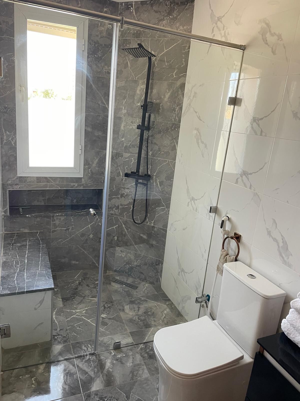 Une salle de bain moderne dotée d’une douche à parois de verre, de toilettes et d’un lavabo.