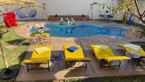 Une piscine avec des chaises longues et une table, entourée d’un jardin agrémenté d’un panneau portant le mot « LOVE ».