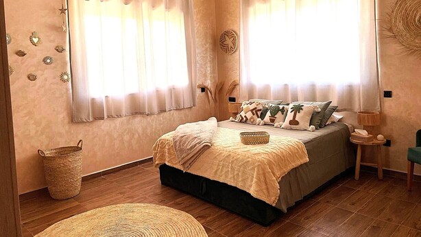 Une chambre à coucher avec un lit, des rideaux, un luminaire suspendu et un élément décoratif mural.