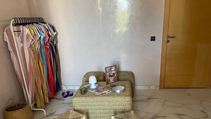 Une pièce comprenant un lit, deux petits tabourets en bois, une lampe, un magazine et un porte-vêtements.