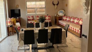 Un espace repas doté d’un sol en marbre, une table centrale entourée de chaises, un canapé agrémenté de coussins à motifs, un téléviseur et une décoration représentant une tête de taureau.