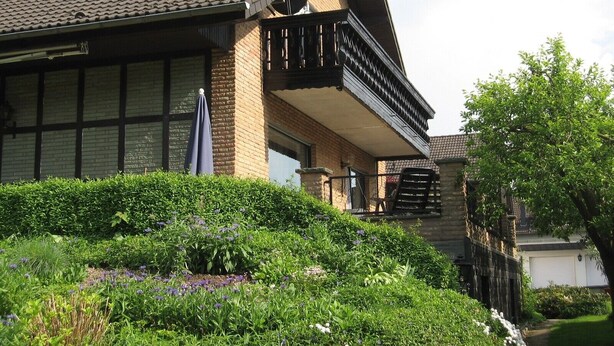 A house with a sloped roof, a balcony, and a garden with various plants and flowers. - Apartment 'Almer' with Balcony and Wi-Fi (Brilon)