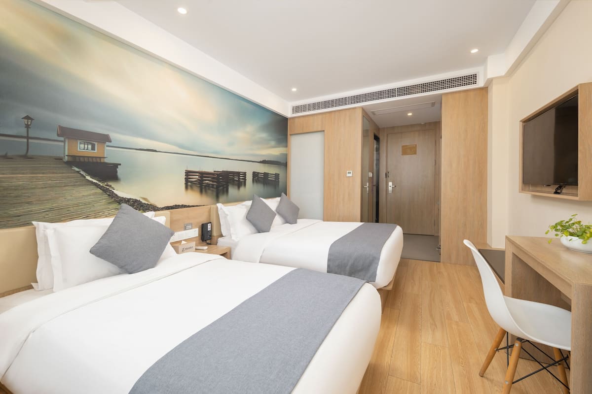 Une chambre d’hôtel avec deux lits, un bureau, une chaise, une télévision et une fresque murale représentant une jetée.