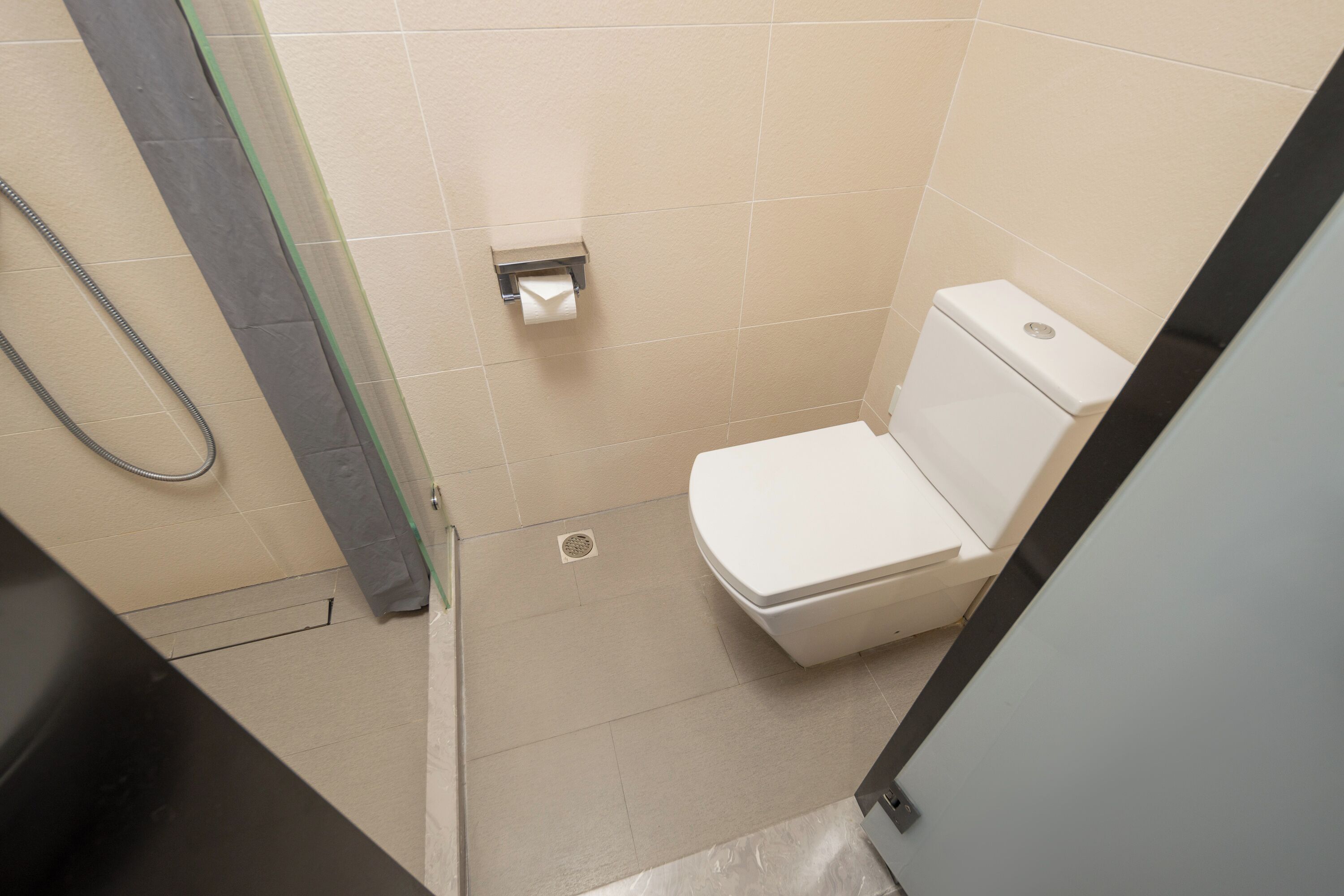 A small, clean bathroom with a toilet, a shower area, and a toilet paper holder.
