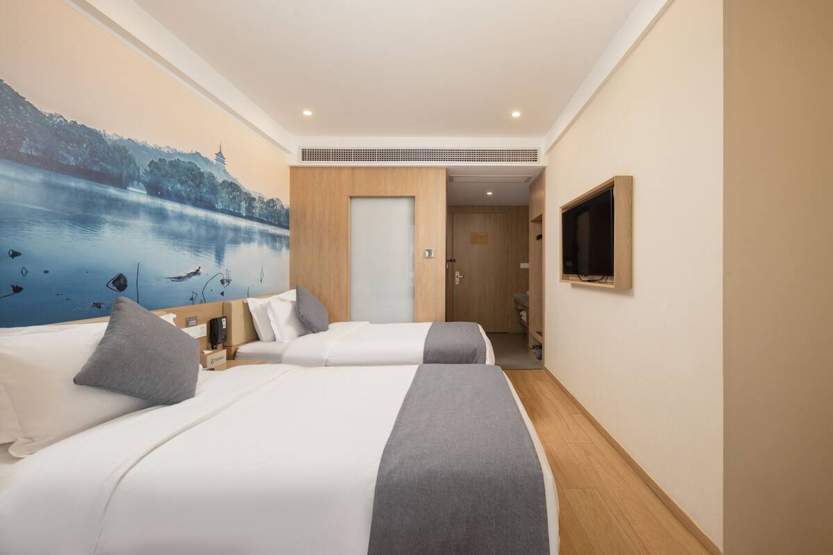 Une chambre d’hôtel avec deux lits, un tableau représentant un lac, une télévision et une porte en bois.