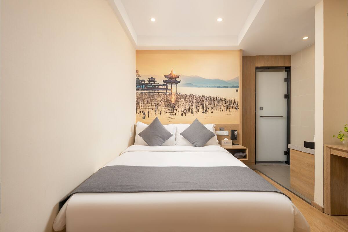 Une chambre d’hôtel moderne dotée d’un grand lit, d’une table de chevet, d’un bureau et d’une fresque murale représentant un bâtiment traditionnel.