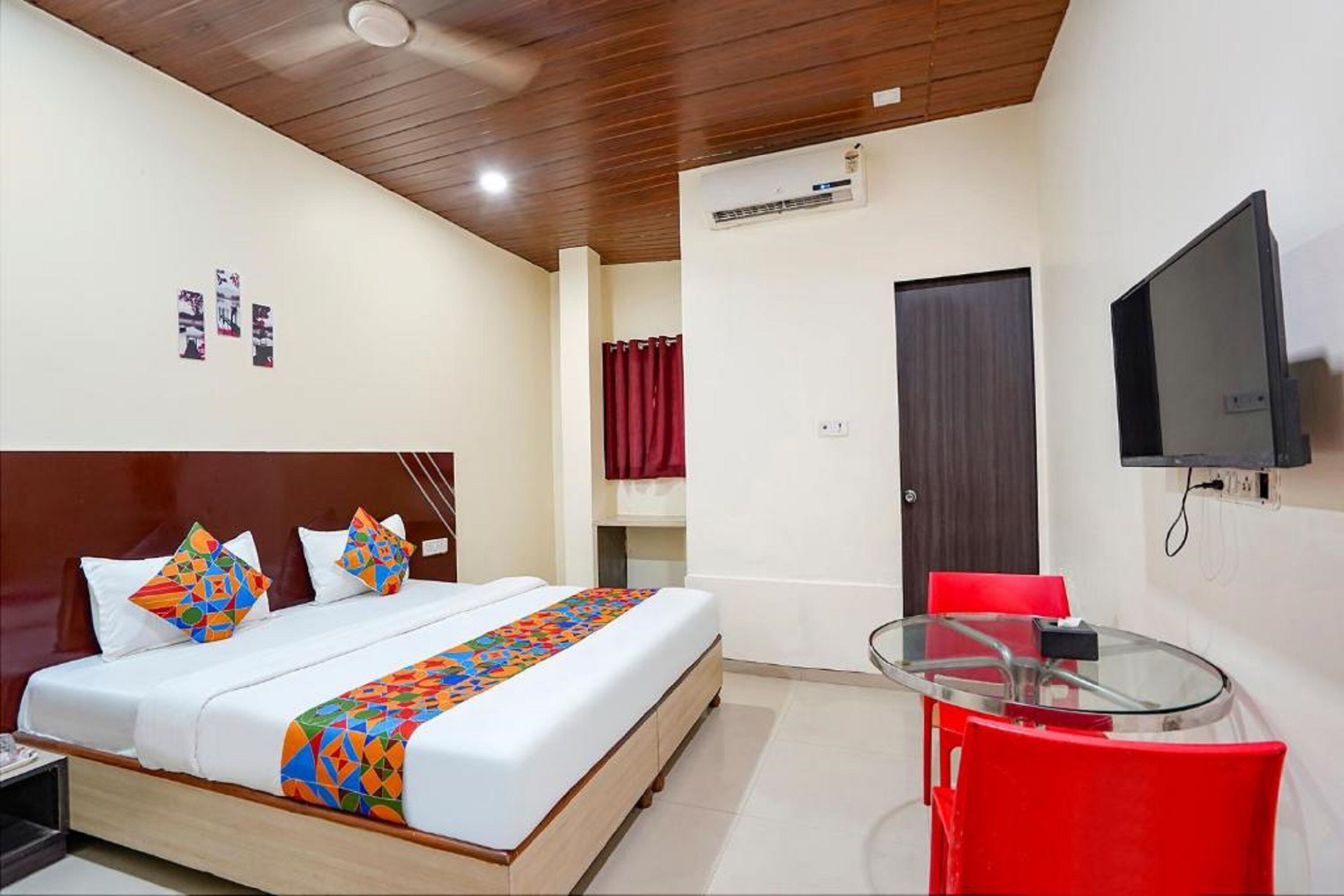 A hotel room with a bed, a TV, a red chair, and a glass table.