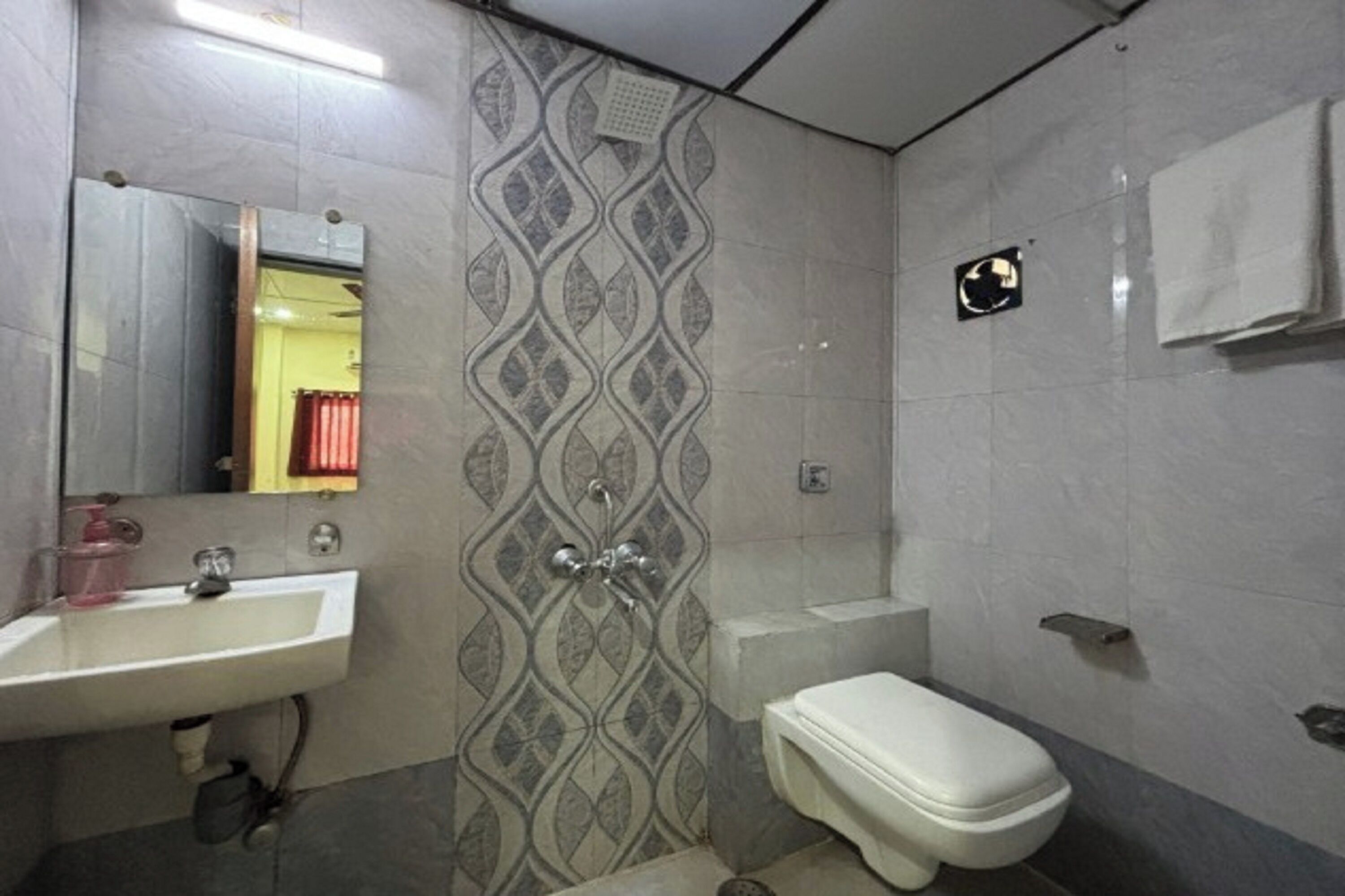 A bathroom with a sink, mirror, toilet, and patterned wall tiles.