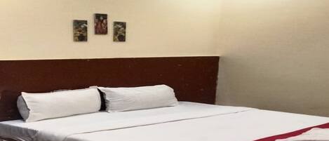 Una cama bien hecha con sábanas blancas y una manta roja, un cabecero de madera y tres pequeños cuadros enmarcados en la pared.