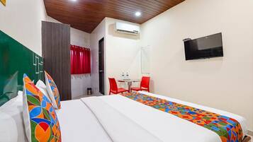A hotel room with two beds, a TV, a small table with chairs, and an air conditioning unit.