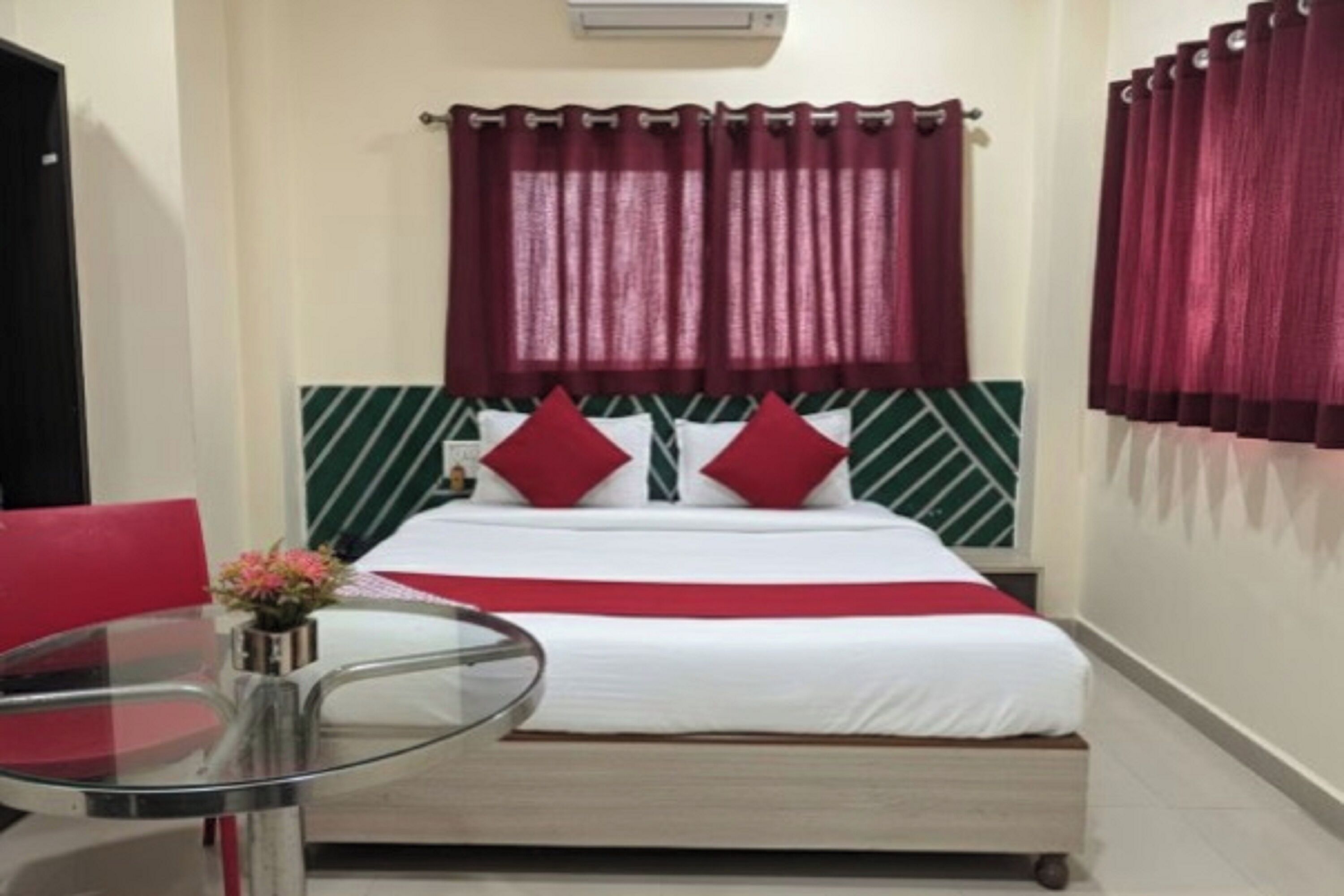 A hotel room with a bed, red curtains, a glass table, and a green and white patterned headboard.