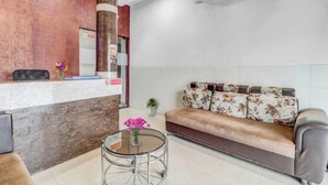 Ein Empfangsbereich mit einem Holzbüro, einem Sofa mit floralen Kissen, einem Glastisch mit Blumenvase und einer Klimaanlage an der Wand.