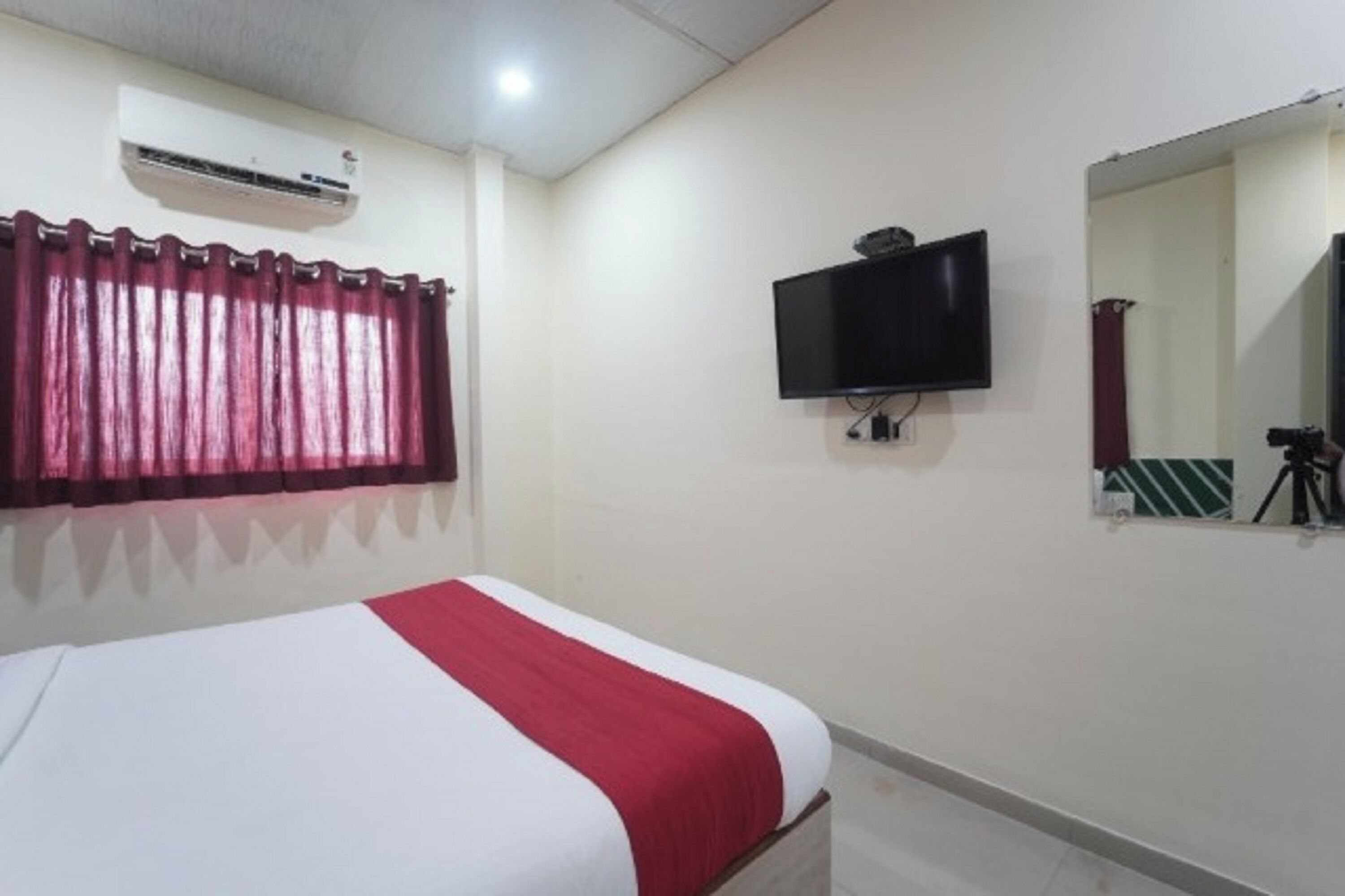 Una habitación de hotel con cama, televisor de pantalla plana, espejo y aire acondicionado.