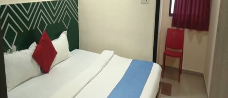 A bed with a white and blue striped bedspread, a green and white patterned headboard, and a red pillow. There is a red chair and a window with red curtains.
