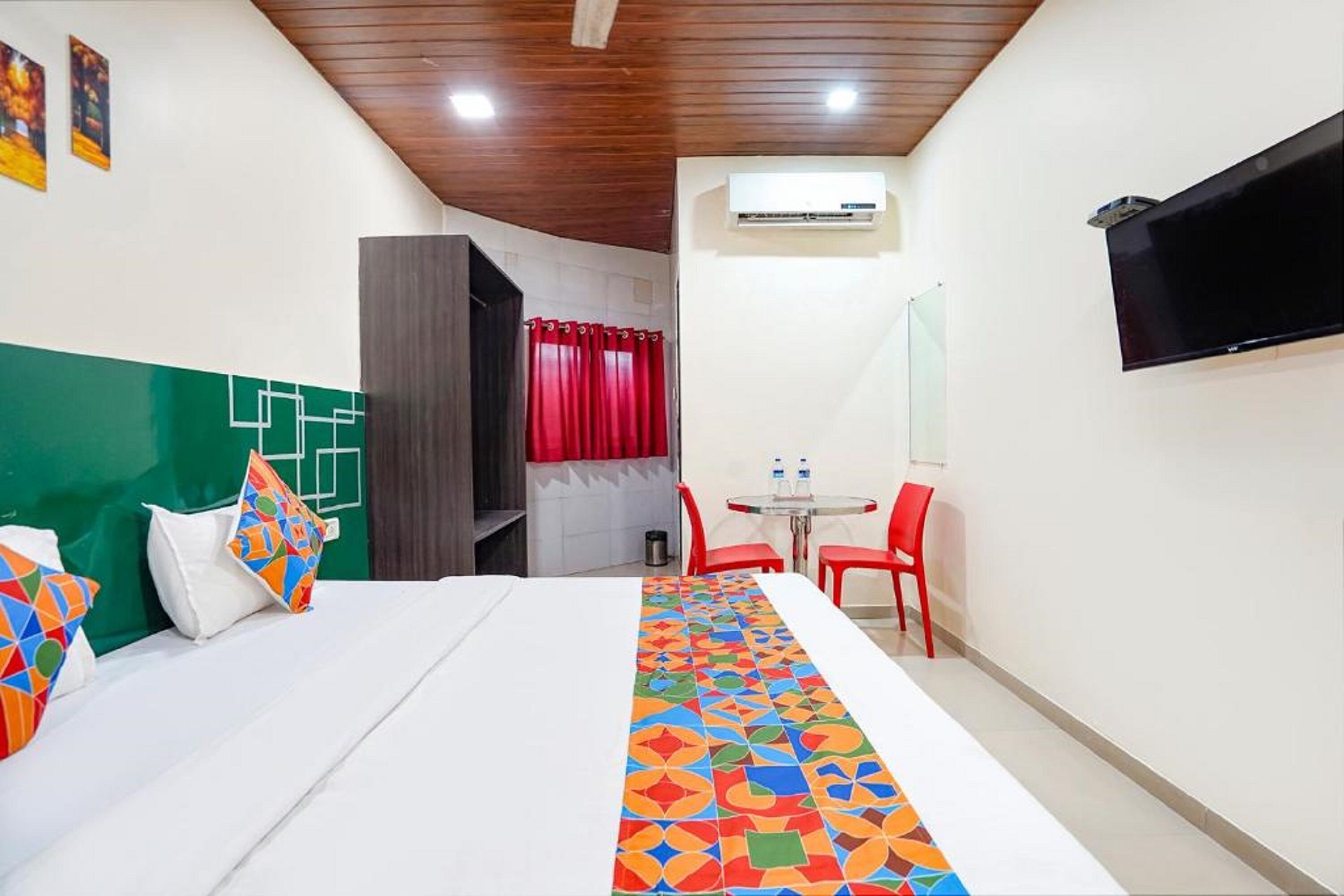 A hotel room with a bed, a small table with chairs, an air conditioning unit, and a television mounted on the wall.