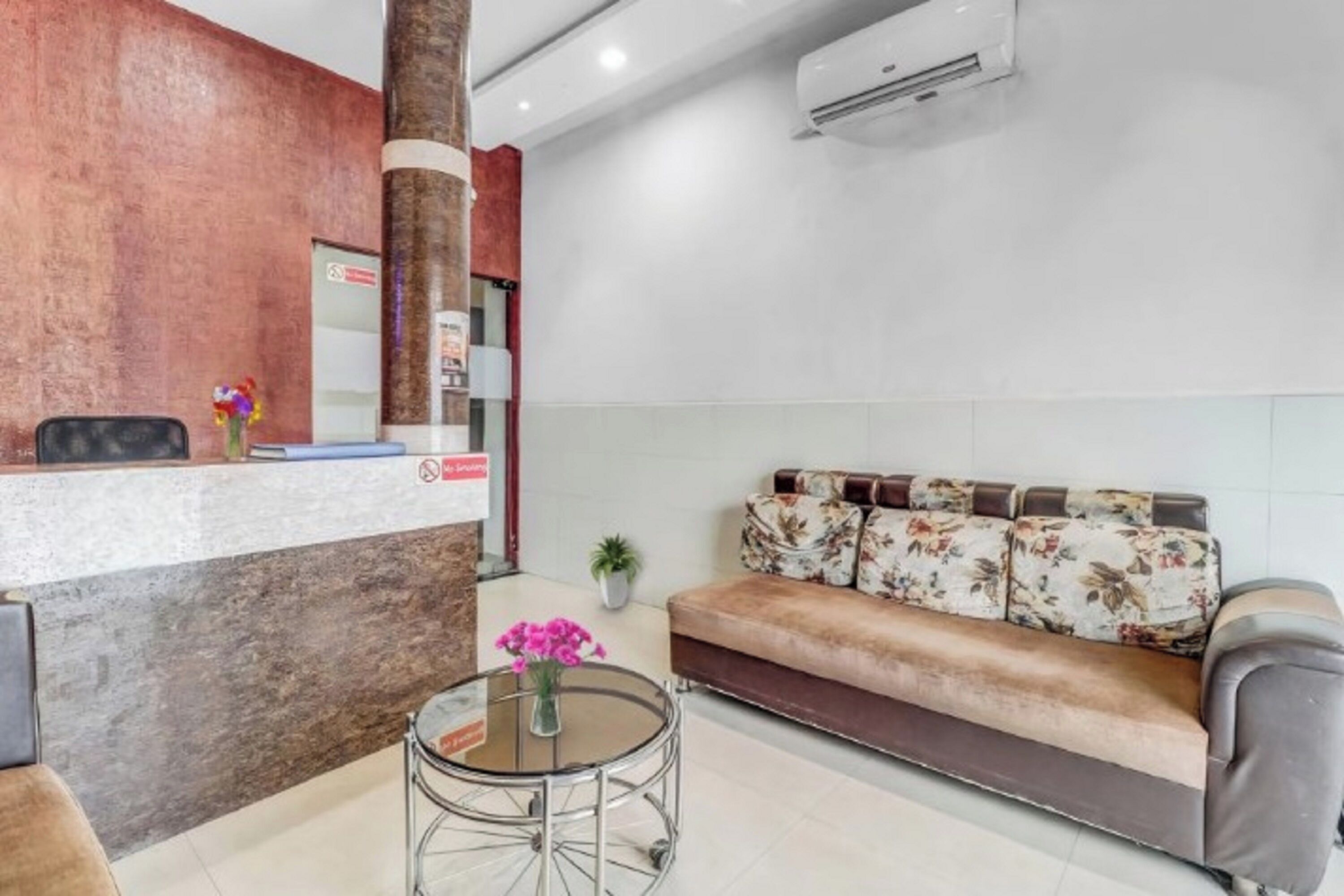 A reception area with a counter, a sofa, a round table with a vase, and a potted plant.