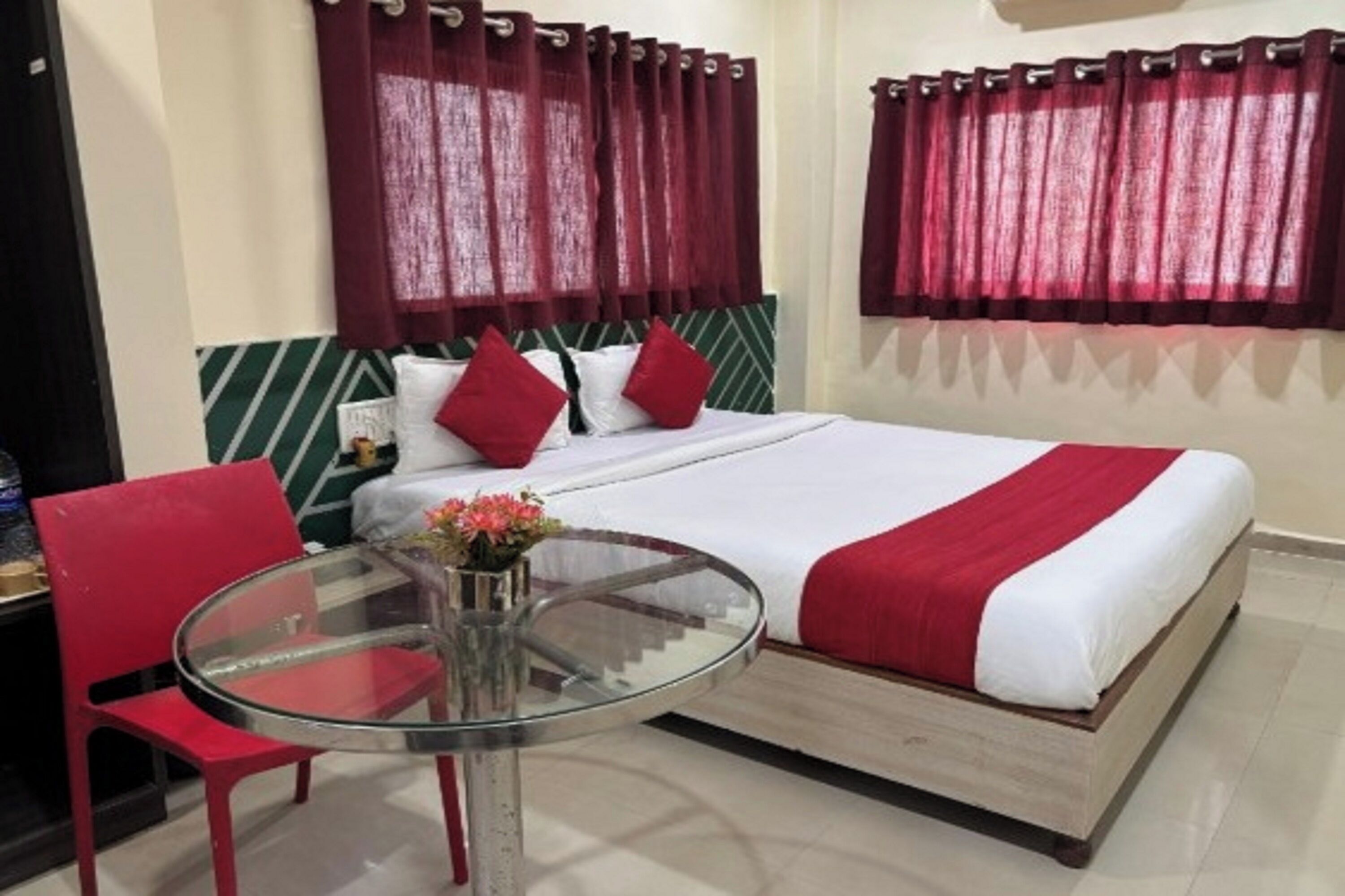 Una camera d'albergo con un letto, tende rosse, un tavolino in vetro e una sedia rossa.