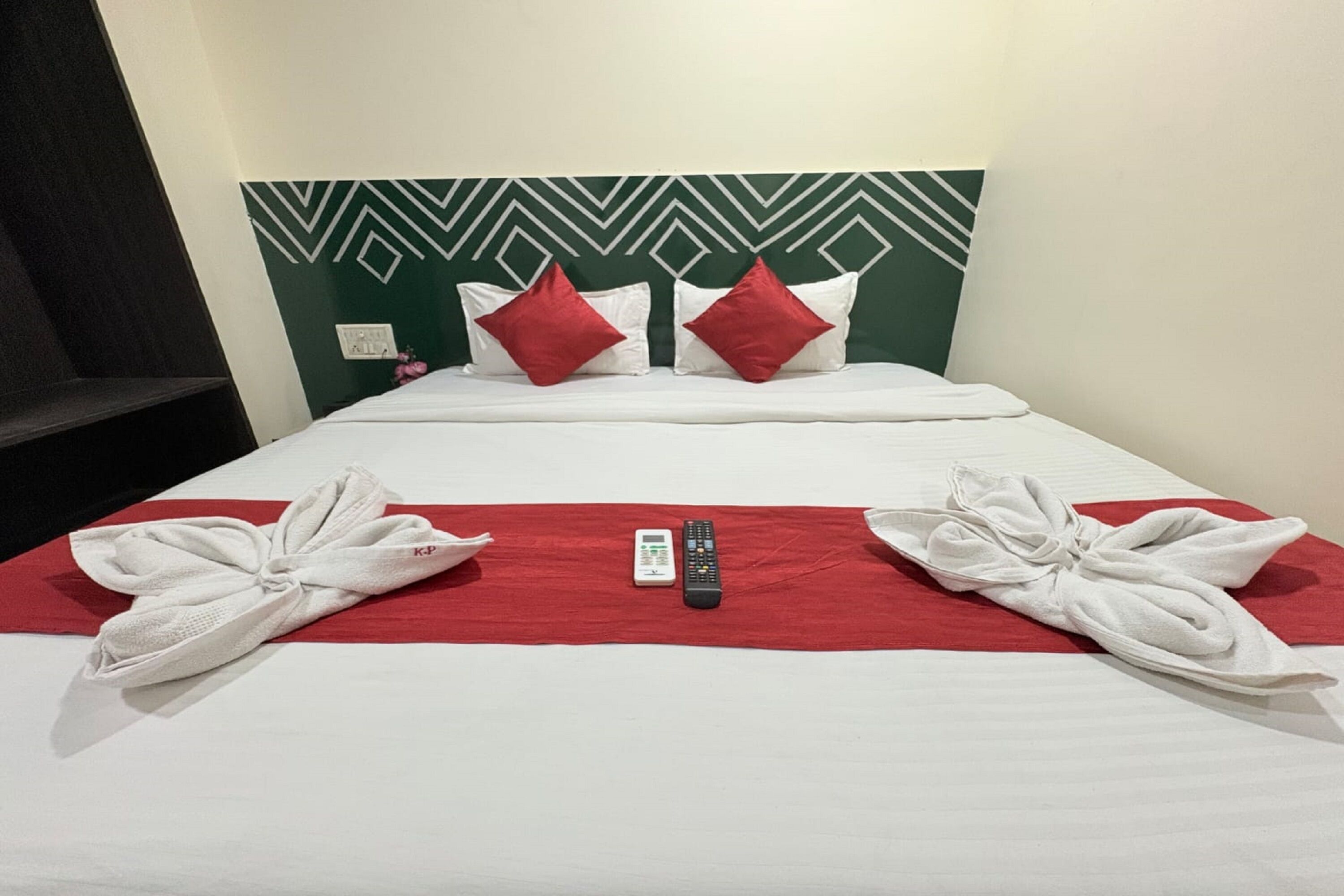 Een hotelkamer met een bed, rode en witte kussens en een afstandsbediening op het bed.
