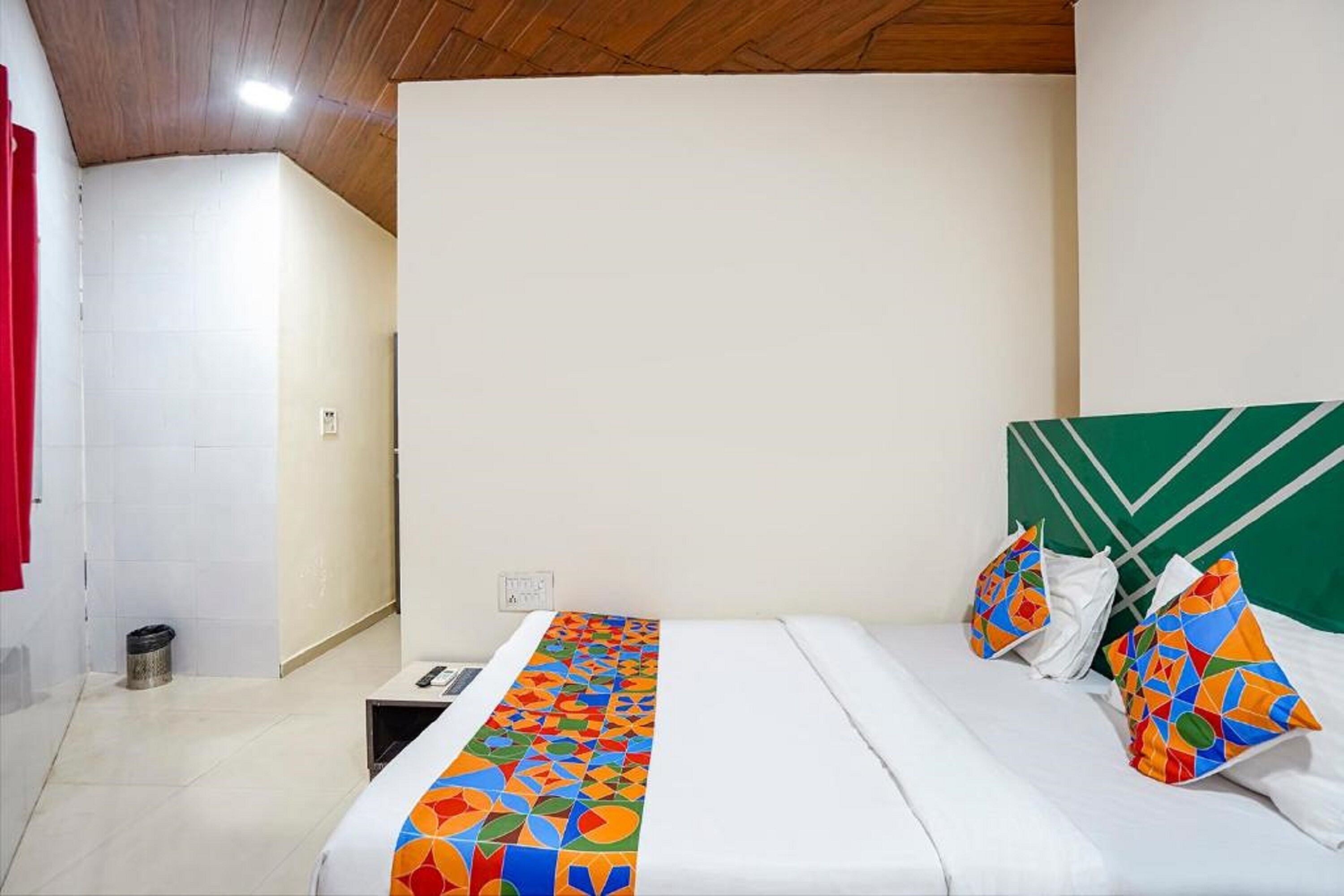 Quarto de hotel com cama, mesa de cabeceira, lixeira e cabeceira verde.
