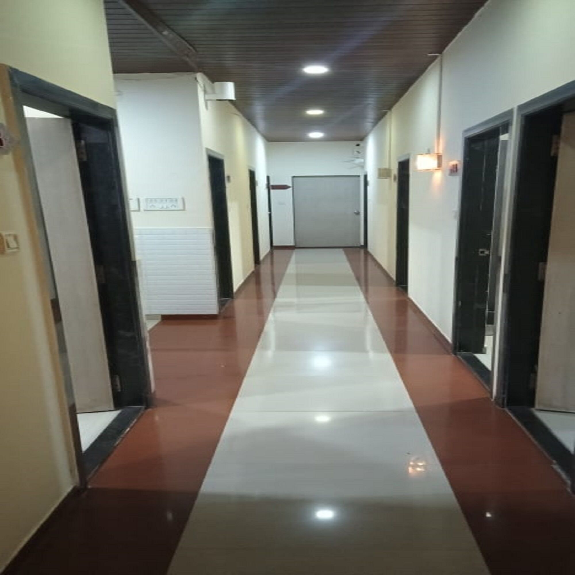 A long, narrow hallway with a shiny floor, doors on both sides, and a door at the end.