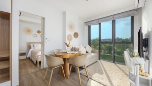 A modern living room with a dining area, a sofa, and a large window offering a city view. - Skypark Aurora Laguna Phuket (Choeng Thale)