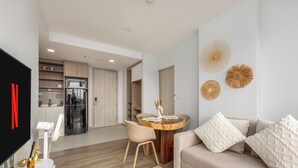 A modern living room with a beige sofa, a round wooden coffee table, and a dining area with a white chair. - Skypark Aurora Laguna Phuket (Choeng Thale)