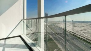 Un bâtiment moderne doté d’un balcon en verre donnant sur une autoroute très fréquentée.