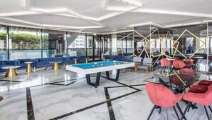 A modern lounge area with a pool table, blue sofas, and red chairs. - 3 Bedroom Apartment at Business Bay - Pool & Spa (Dubai)