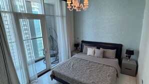 A bedroom with a large bed, a chandelier, a nightstand, and a view through a glass door. - 3 Bedroom Apartment at Business Bay - Pool & Spa (Dubai)
