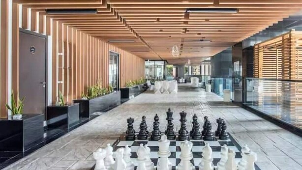 A modern hotel corridor with a chessboard set up on the floor, wooden paneling on the walls, and a glass railing on one side. - 3 Bedroom Apartment at Business Bay - Pool & Spa (Dubai)
