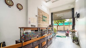 A reception area with a wooden reception desk, two wall clocks, and a large window overlooking a street. - Collection O Dinh Dinh Hotel - Near Tan Son Nhat Airport (Ho Chi Minh City)
