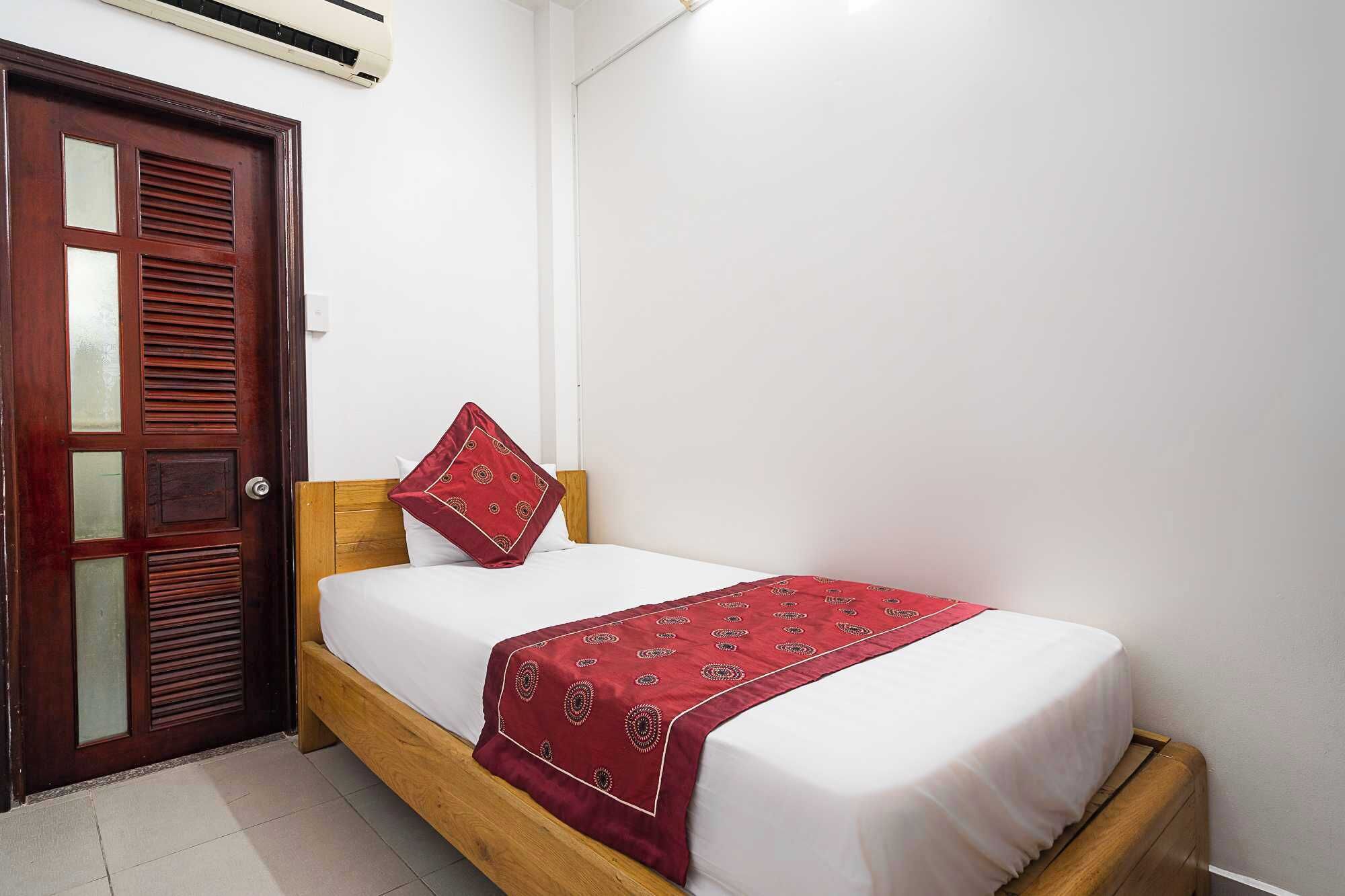 A single bed with a wooden frame, a red patterned throw, and a white mattress.