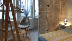 Et soveværelse med seng, stol, lille bord og en væg med et struktureret mønster.