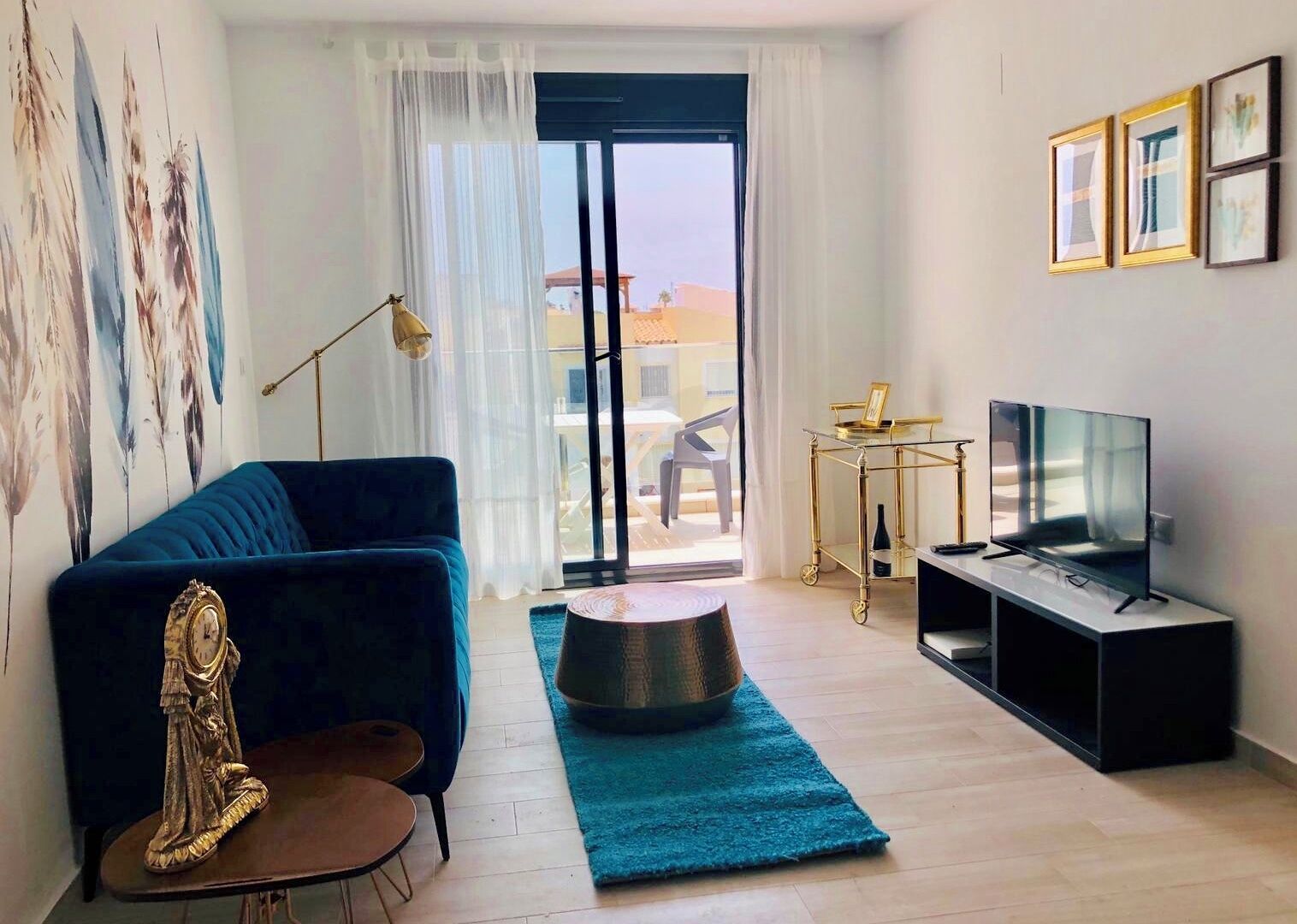Un salón moderno con un sofá azul, una estatua, un televisor y vistas a través de un ventanal.