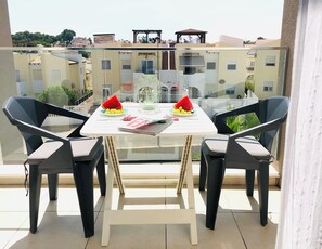 A balcony with a glass table, two chairs, a watermelon, and a magazine.