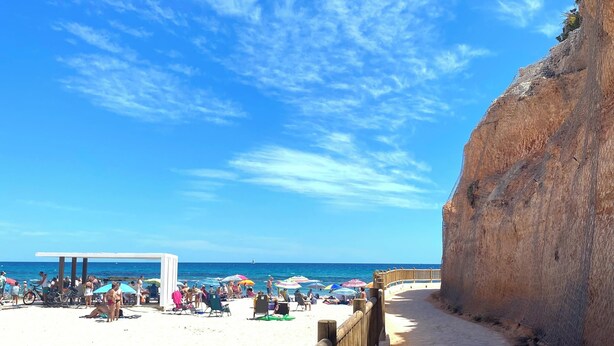 A beach with a wooden walkway and a rocky cliff. - Modern 2 Bedroom Apartment in Villamartin 3 Pools, Padel, Jacuzzi Sandy Beaches (Villamartín)