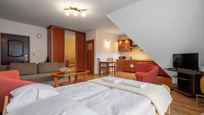 A modern hotel room with a large bed, a sofa, a dining table, and a kitchen area. - RentPlanet - Za Cieszynianką (Zakopane)