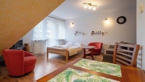 A bedroom with a bed, a red chair, a wooden table, and a ceiling light fixture. - RentPlanet - Za Cieszynianką (Zakopane)