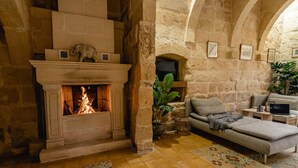 Une pièce aux murs de pierre, avec une cheminée, un canapé et un ordinateur portable posé sur une table d’appoint.