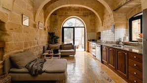 Un intérieur chaleureux avec une arche en pierre, un canapé, une cuisine dotée de meubles en bois et un mur recouvert de carreaux.