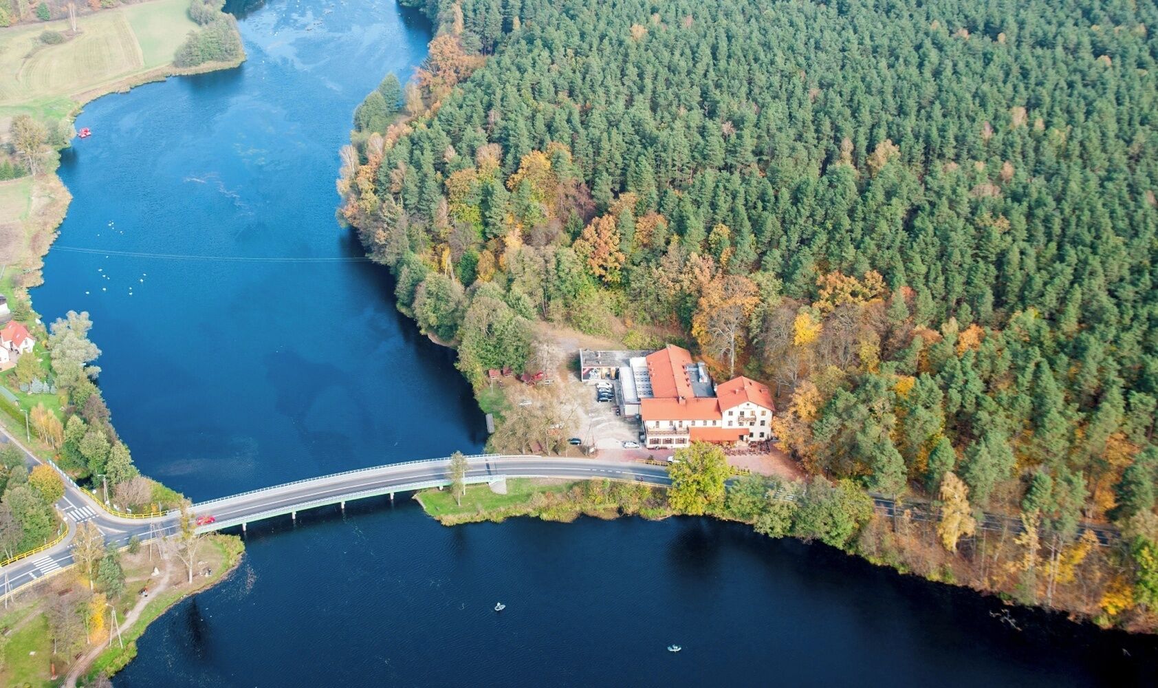 An aerial view of a riverside property with a bridge, a forested area, and a building with a red roof.