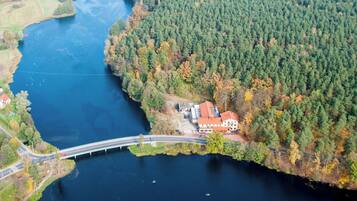 An aerial view of a riverside property with a bridge, a forested area, and a building with a red roof.